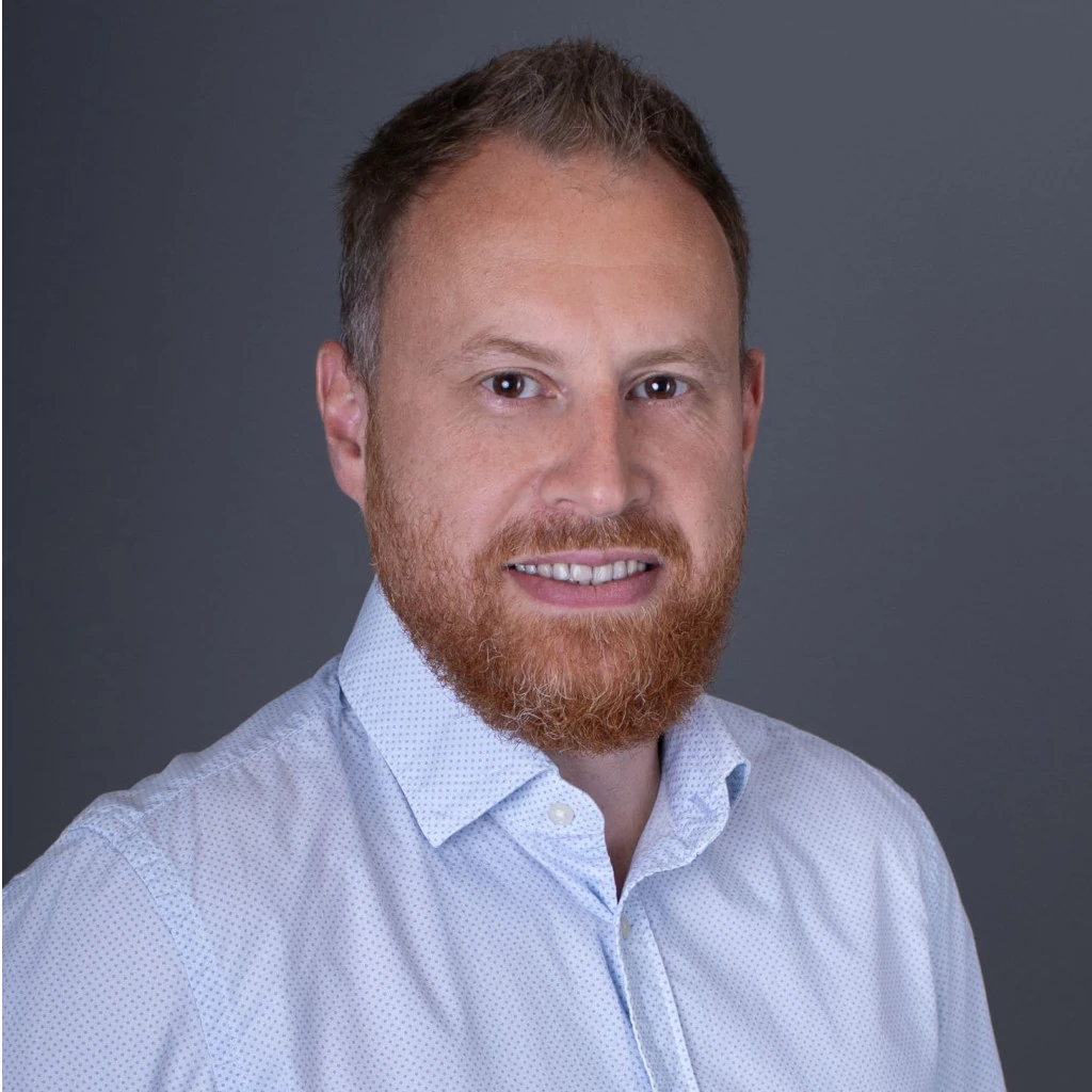 Profilbild vom Geschäftsführer Sergej Brack. Sergej Brack in einem hellblauen Hemd vor einem neutralen dunkelgrauen Hintergrund. Die Atmosphäre ist formell und professionell, Sergej Brack wirkt ruhig und selbstbewusst.